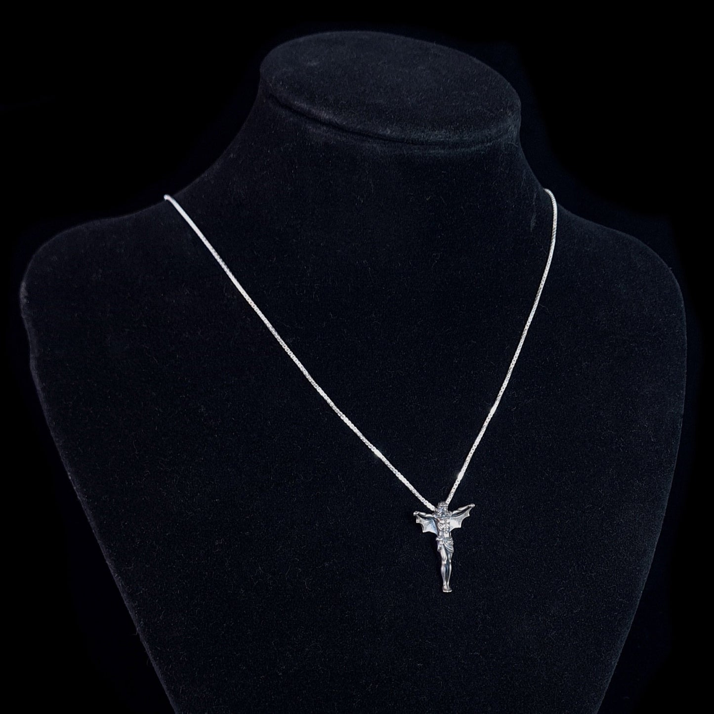 Sterling silver Bat Jesus pendant by RBZ Jewelry displayed on a black velvet mannequin bust, showing the gothic crucifix with bat wings on a fine silver chain to illustrate how the piece sits when worn.