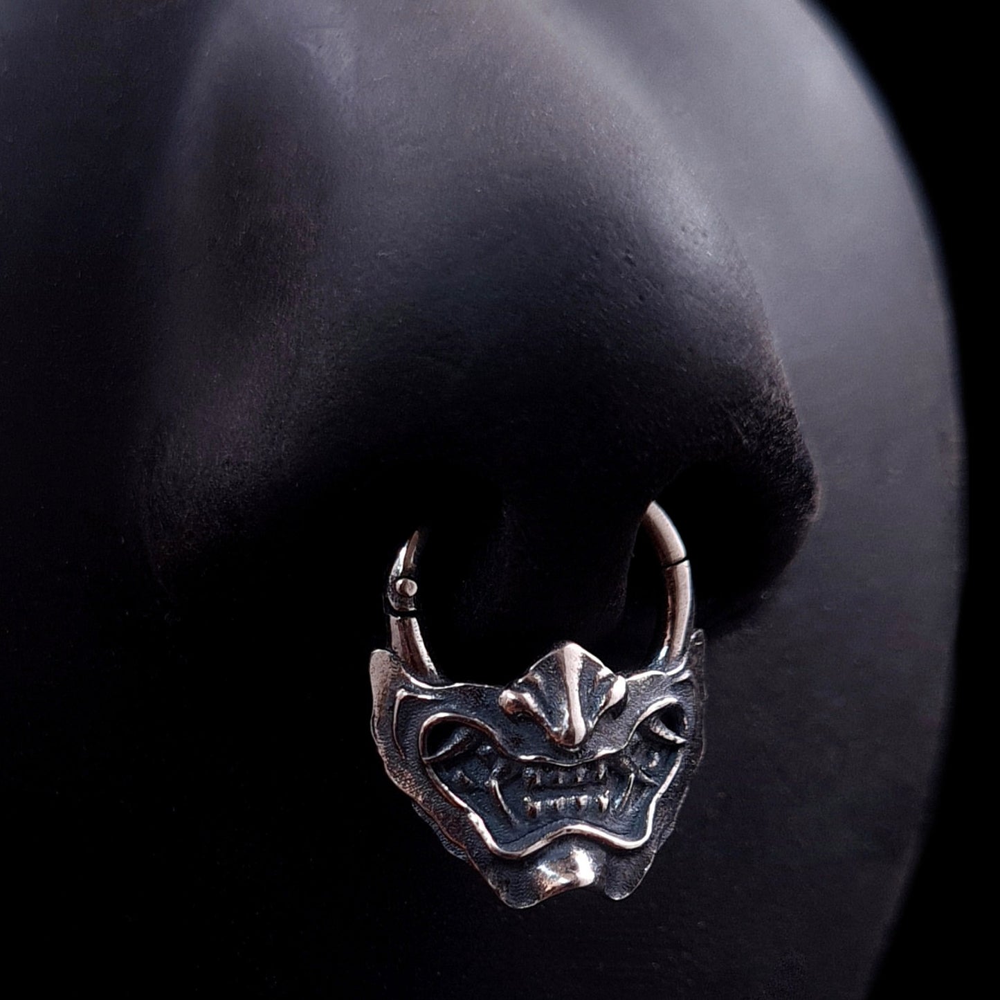 Sterling silver Samurai Oni mask septum ring by RBZ Jewelry, shown worn on a life-size black silicone nose model to demonstrate fit and appearance.