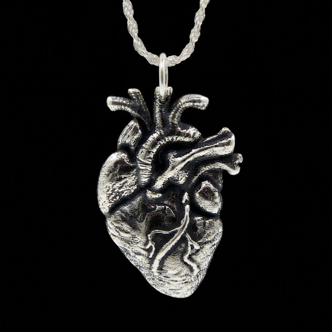 Highly detailed sterling silver anatomical heart pendant by RBZ Jewelry featuring realistic chambers, valves, and arteries with a high-contrast oxidized finish, shown on a silver chain against a black background.