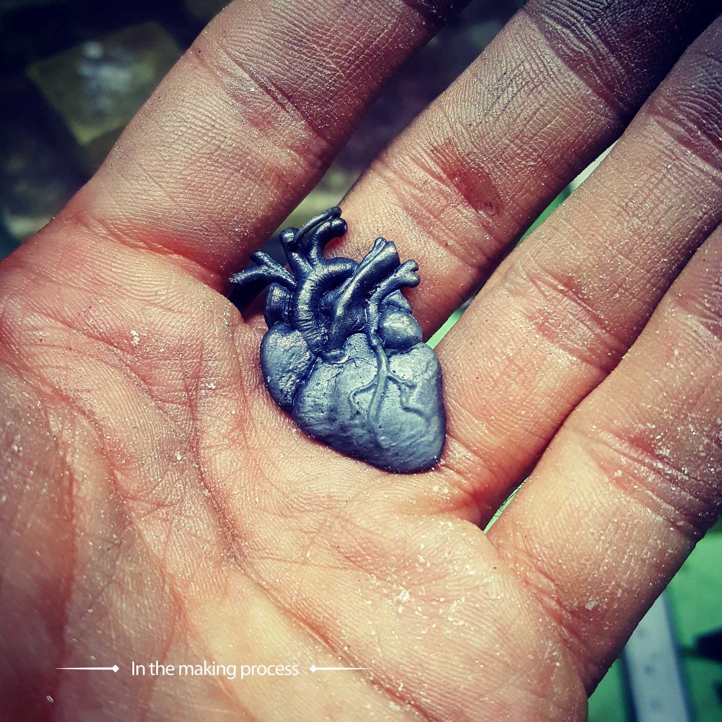 A fully oxidized sterling silver anatomical heart pendant by RBZ Jewelry resting in a jeweler's hand during the making process, emphasizing the raw biological details and artisanal craftsmanship.