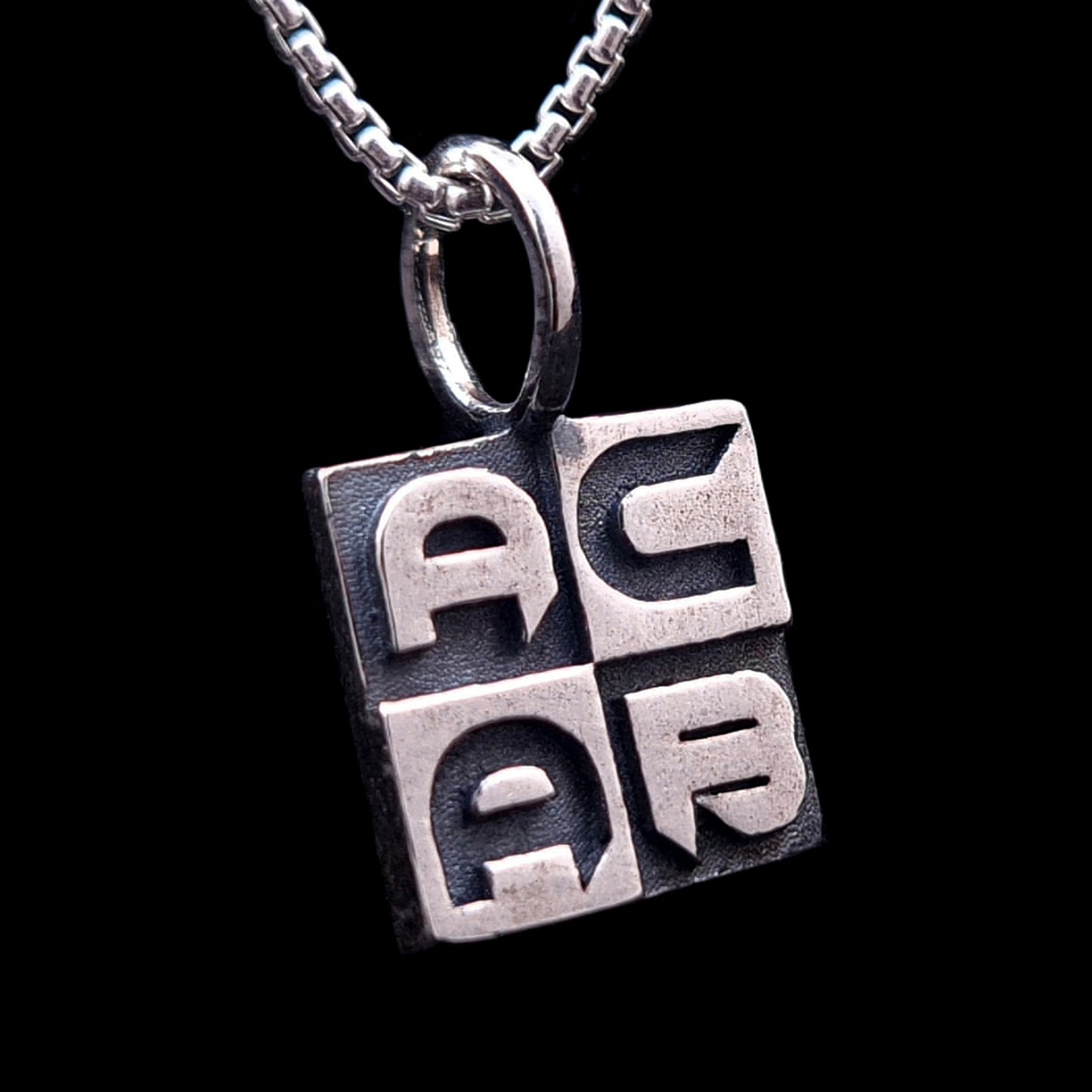 Brutalist-style sterling silver ACAB pendant featuring heavy block-letter engraving and an oxidized antique finish, hanging from a silver box chain, by RBZ Jewelry.