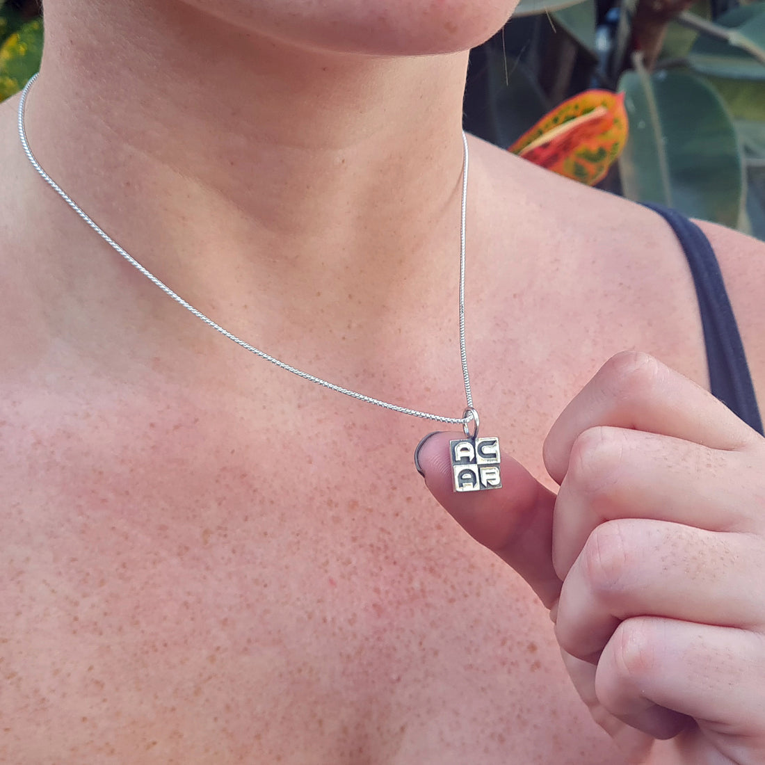 Close-up lifestyle view of the sterling silver ACAB pendant worn by a model, demonstrating its compact scale and the sharp detail of the brutalist block-lettering.
