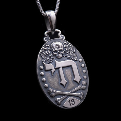 Gothic Judaica sterling silver Chai pendant by RBZ Jewelry, featuring high-relief Hebrew letters חי, a detailed skull engraved with a Star of David, vine leaves, crossed bones, and the number 18 plaque on a deeply oxidized oval medallion.