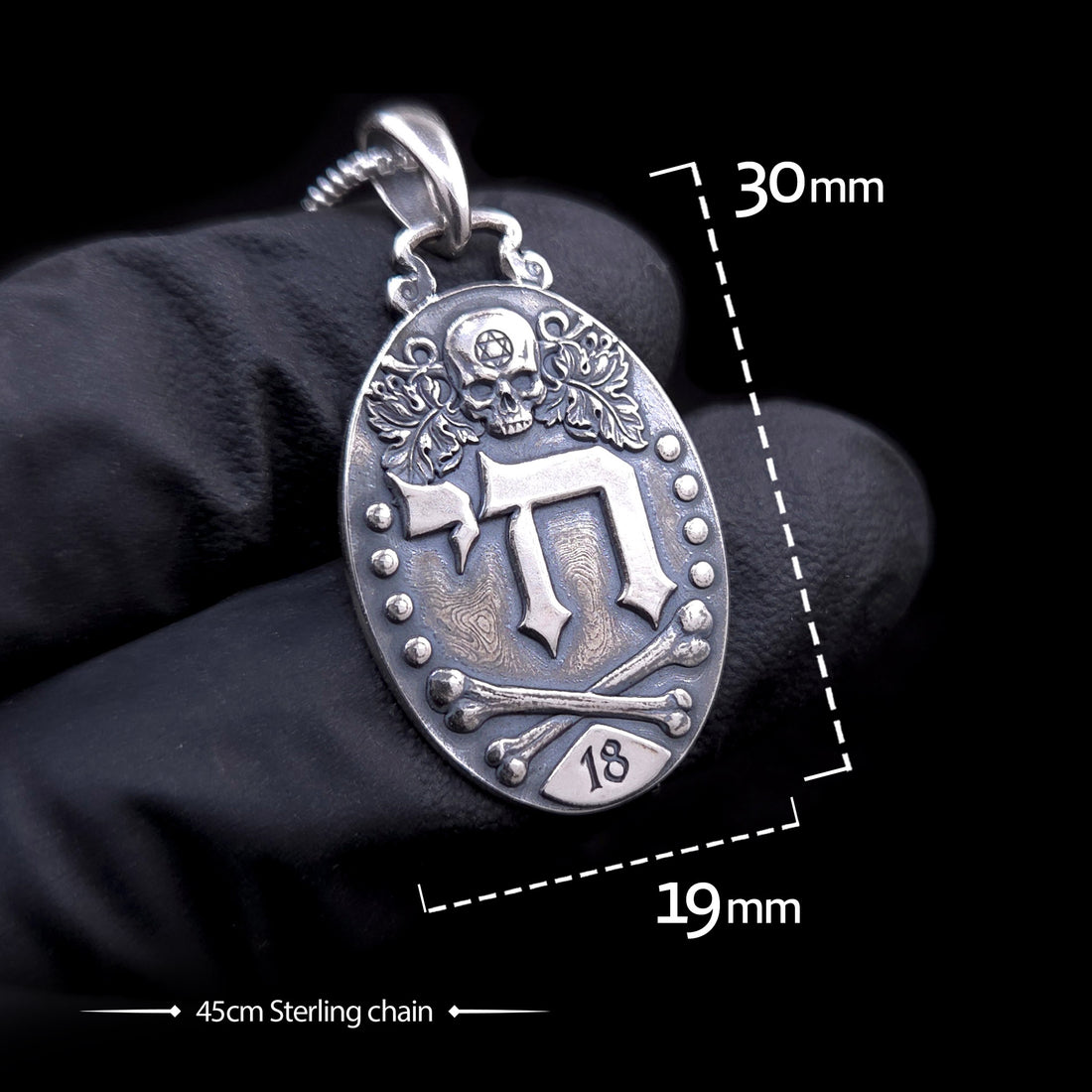 Gothic Judaica sterling silver Chai pendant by RBZ, held in a black-gloved hand for scale, featuring dimension overlays of 30mm height by 19mm width and a 45cm sterling silver chain.