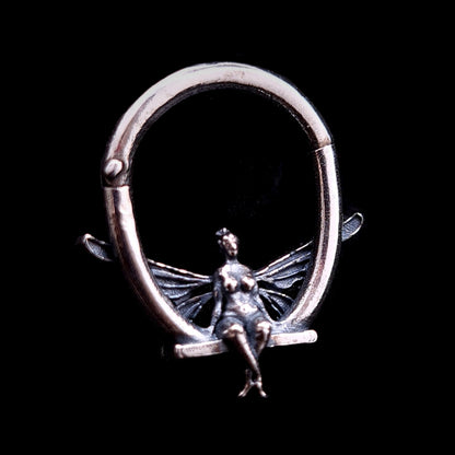 Handcrafted RBZ Jewelry enchanted fairy septum ring in oxidized sterling silver. The design features a miniature fairy resting on a swing, showcasing the brand's signature gothic fantasy aesthetic.