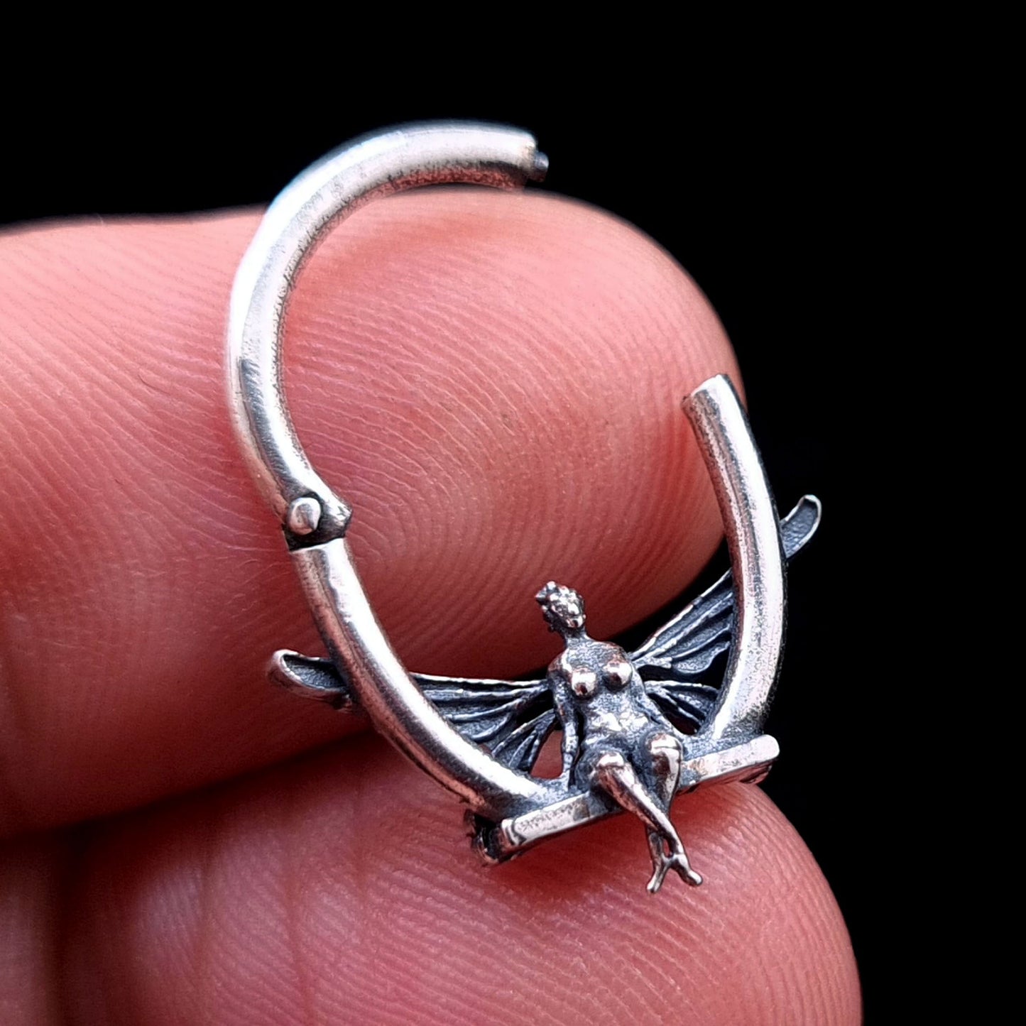 Solid 925 sterling silver fairy septum clicker shown in the open position, held between fingers to demonstrate scale and detailed 3D proportions, by RBZ Jewelry.