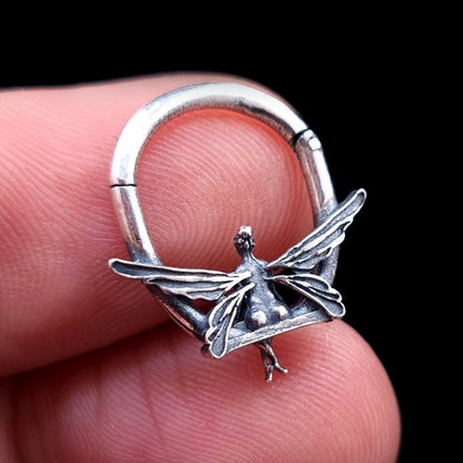Solid 925 sterling silver fairy septum clicker shown from the back in the closed position, held between fingers to demonstrate scale and detailed 3D wing textures.