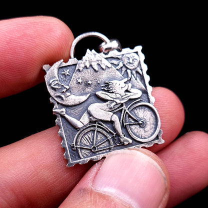 Sterling silver Bicycle Day blotter necklace, held in fingers to show its small, detailed size