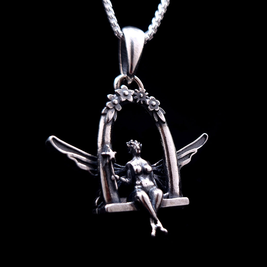 Sterling silver Flower Fairy pendant by RBZ Jewelry, featuring an intricately detailed fairy with spread wings sitting on a floral-arched swing and holding a star-tipped wand against a black background.