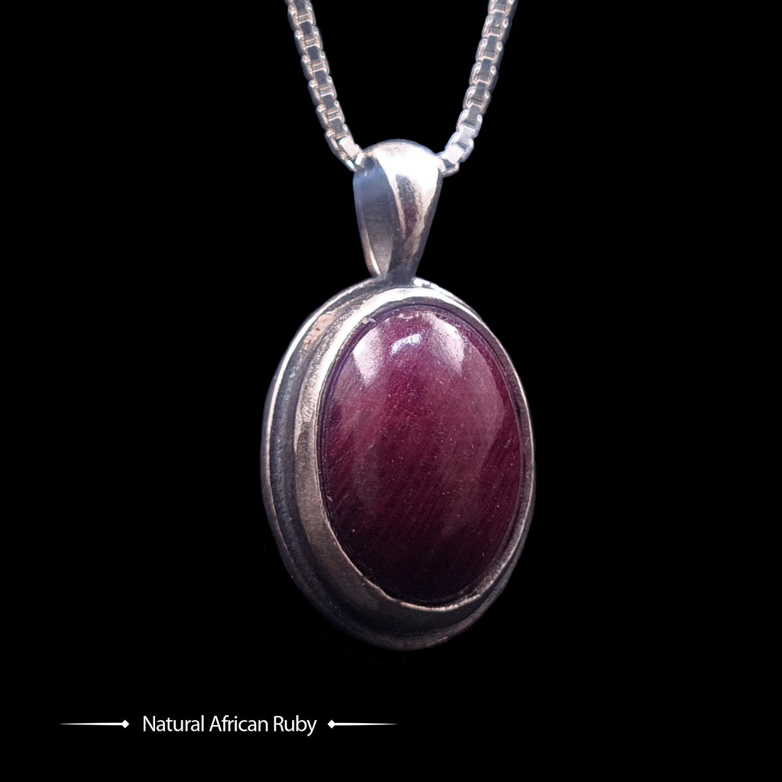 Studio-crafted RBZ Jewelry Gothic pendant featuring a deep purple-red Natural African Ruby cabochon encased in a polished Sterling silver bezel, front view of the double-sided Skull Bezel design on a silver box chain.