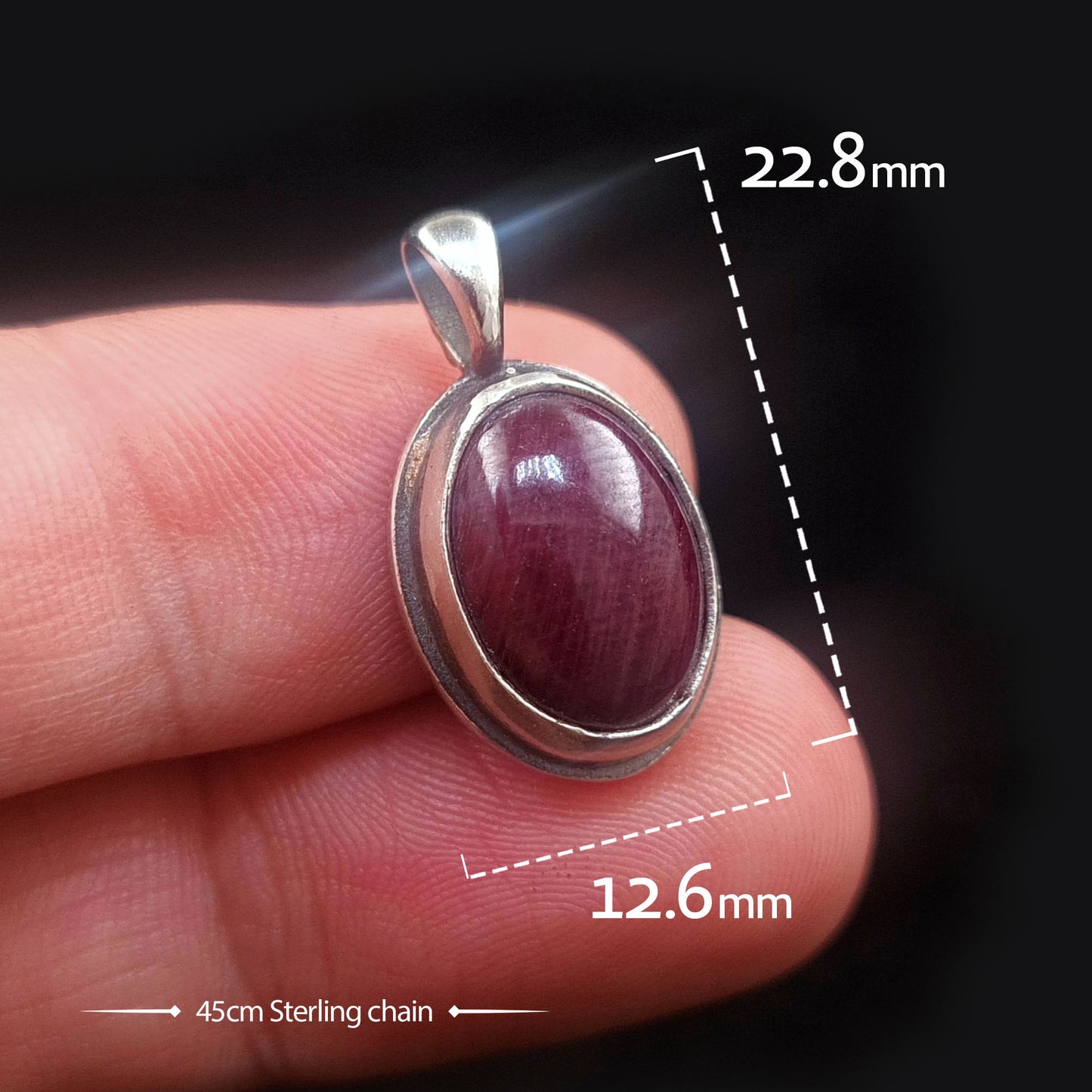 Studio-crafted RBZ Jewelry Gothic pendant held between fingers for scale, showcasing the 22.8mm by 12.6mm Sterling silver skull bezel with a Natural African Ruby, including reference to a 45cm Sterling chain.