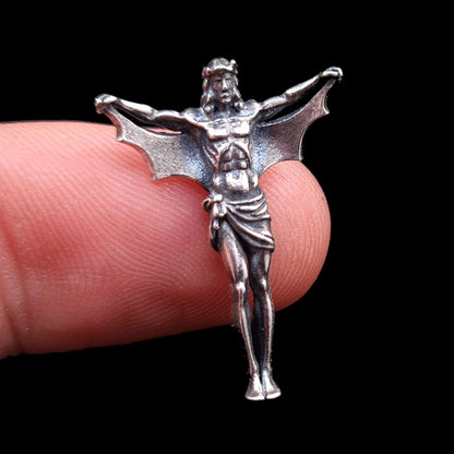 Front view of the sterling silver Bat Jesus pendant by RBZ Jewelry held on a finger for scale, highlighting the miniature anatomical gothic details and textured bat wings against a black background.
