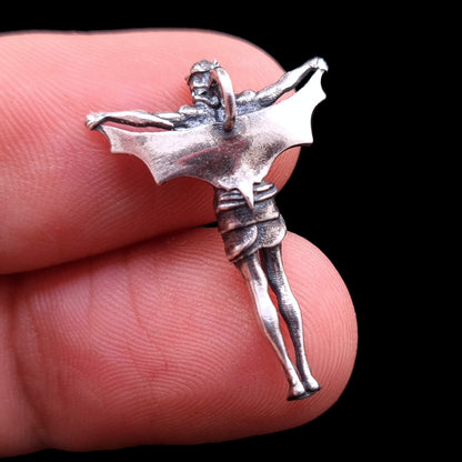 Rear view of the sterling silver Bat Jesus pendant by RBZ Jewelry, held between two fingers to show its small scale. The image highlights the smooth oxidized back of the bat wings, the anatomical details of the legs and loincloth, and the integrated silver bail for a chain.