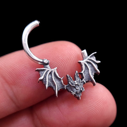 Studio-crafted RBZ Jewelry Gothic Sterling silver Glitched Bat septum clicker ring shown in an open position while held between fingers. The image highlights the visceral, distorted bat silhouette and oxidized textured wings of the studio-crafted piece against a black background.