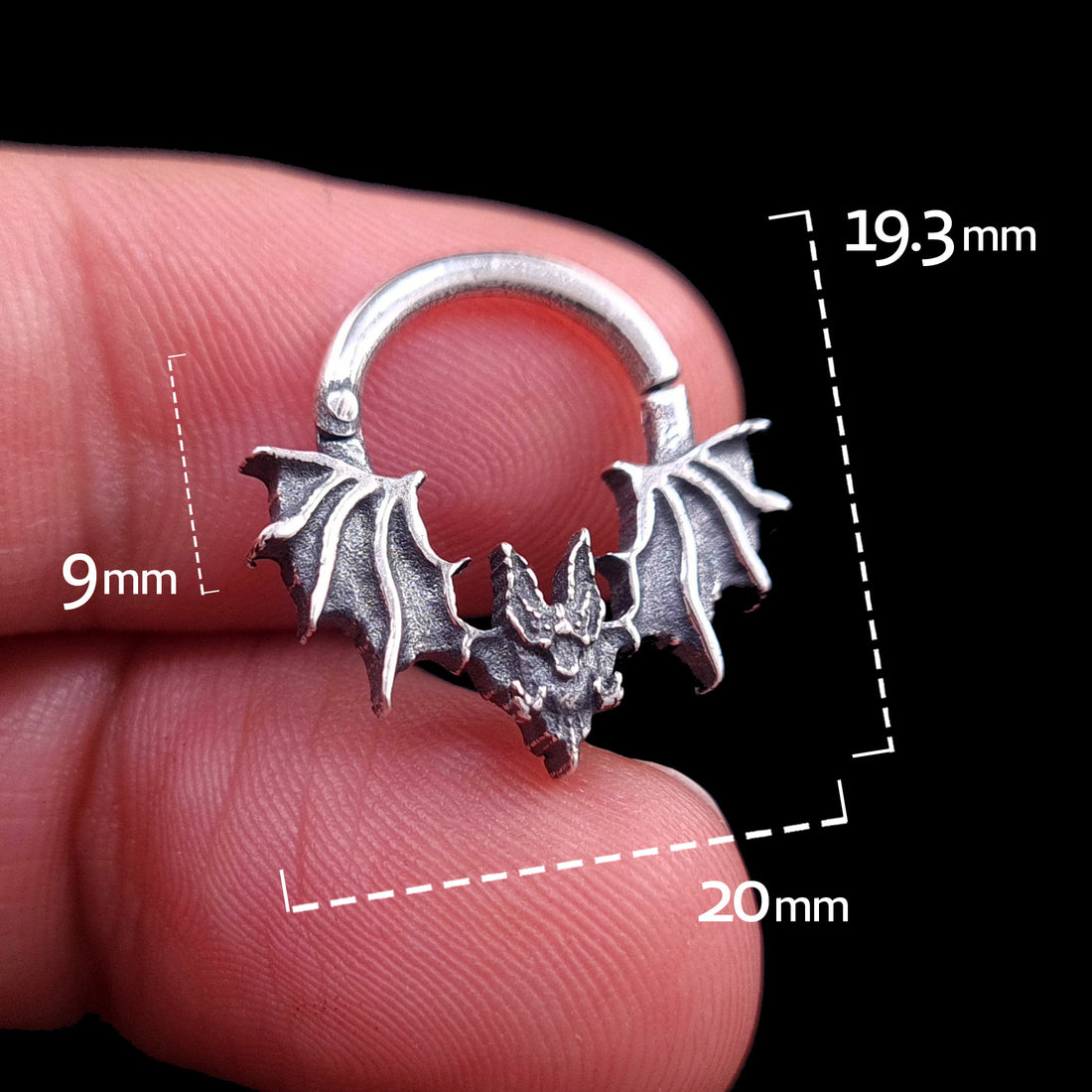 Front view of the studio-crafted RBZ Jewelry Gothic Sterling silver Glitched Bat septum clicker ring held in hand for scale. The image features technical measurement overlays showing a 20mm width, 19.3mm total height, and 9mm nose drop. This visceral, distorted bat silhouette is isolated against a solid black background.