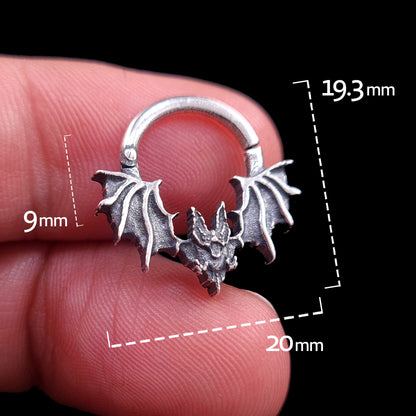Front view of the studio-crafted RBZ Jewelry Gothic Sterling silver Glitched Bat septum clicker ring held in hand for scale. The image features technical measurement overlays showing a 20mm width, 19.3mm total height, and 9mm nose drop. This visceral, distorted bat silhouette is isolated against a solid black background.