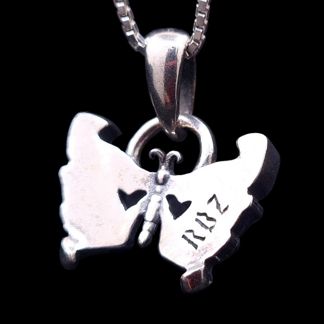 The back side of the Sterling silver Gothic Butterfly Skull pendant by RBZ Jewelry, featuring the RBZ logo engraving, two heart-shaped cutouts, and a polished finish against a black background.