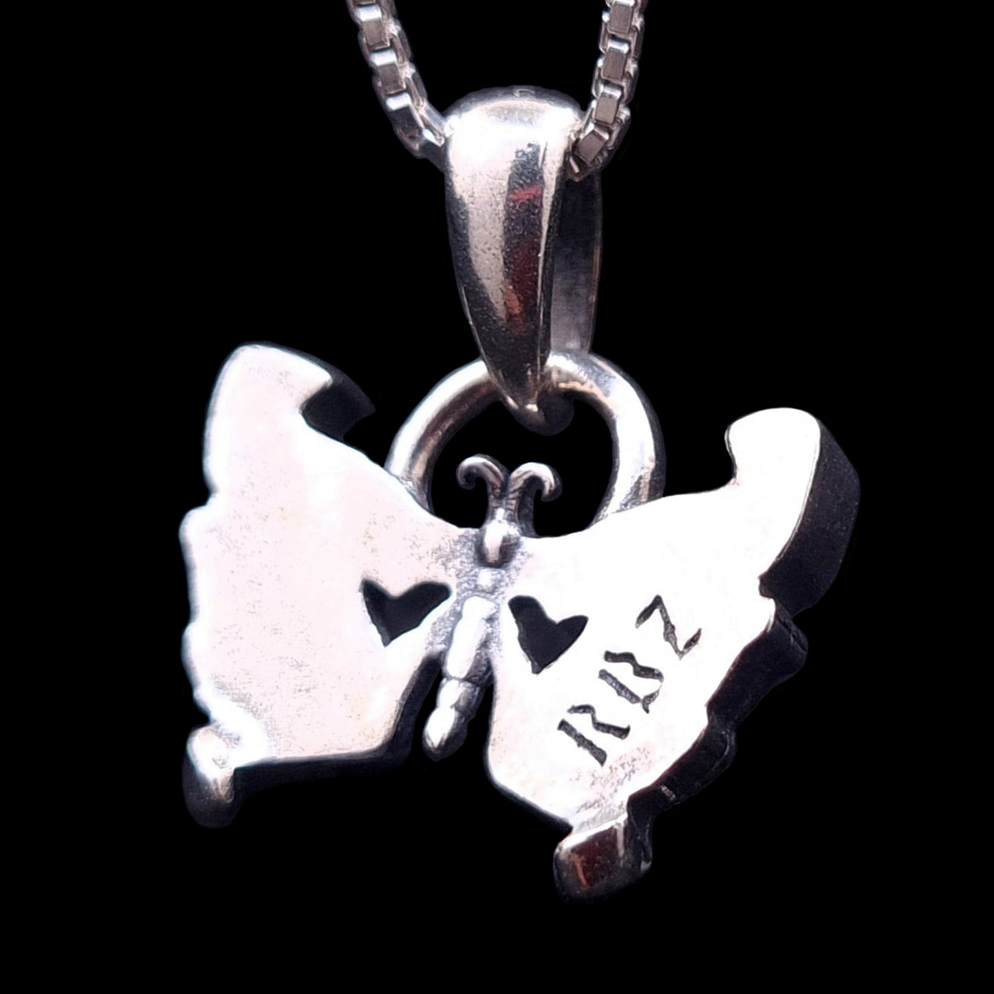 The back side of the Sterling silver Gothic Butterfly Skull pendant by RBZ Jewelry, featuring the RBZ logo engraving, two heart-shaped cutouts, and a polished finish against a black background.