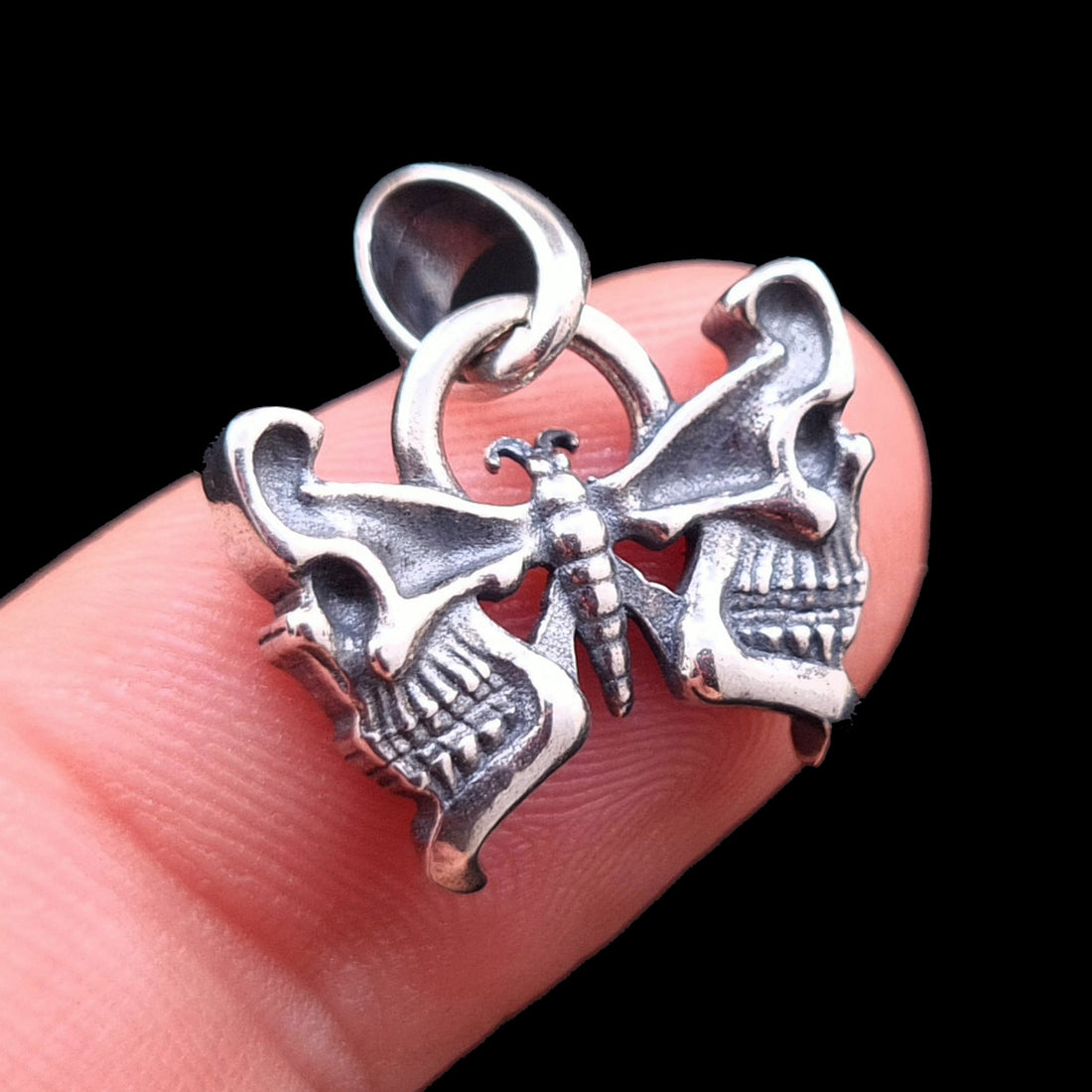 RBZ Jewelry Sterling silver Gothic Butterfly Skull pendant held on a finger for size reference, featuring the detailed anatomical skull wing design and dark Memento Mori aesthetic against a black background.