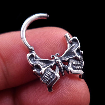 Sterling silver Gothic butterfly skull septum clicker ring by RBZ Jewelry, shown in the open position while held between fingers to demonstrate the hinge mechanism and scale.