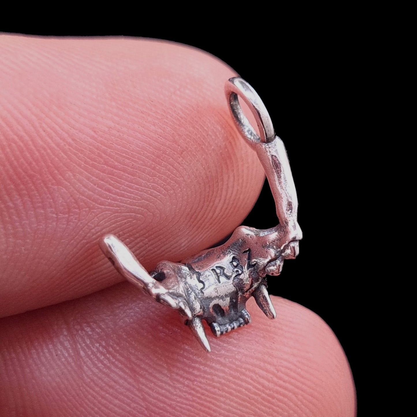 Rear view of the RBZ Jewelry Sterling silver Gothic Cat Skull Jawbone pendant held on a finger for scale, showcasing the RBZ logo engraving and the anatomical skeletal texture against a black background.