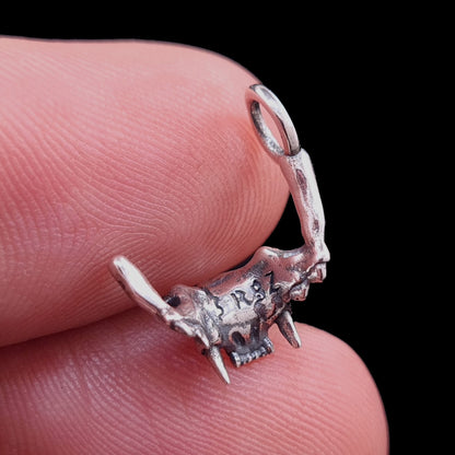 Rear view of the RBZ Jewelry Sterling silver Gothic Cat Skull Jawbone pendant held on a finger for scale, showcasing the RBZ logo engraving and the anatomical skeletal texture against a black background.