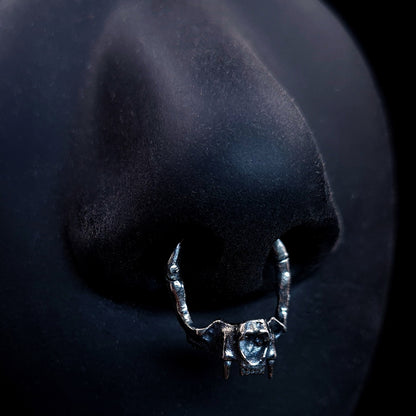 Product shot of the RBZ Jewelry sterling silver cat skull septum clicker ring worn on a life-size matte black silicone nose, demonstrating the fit and anatomical bone texture of the gothic predator design.