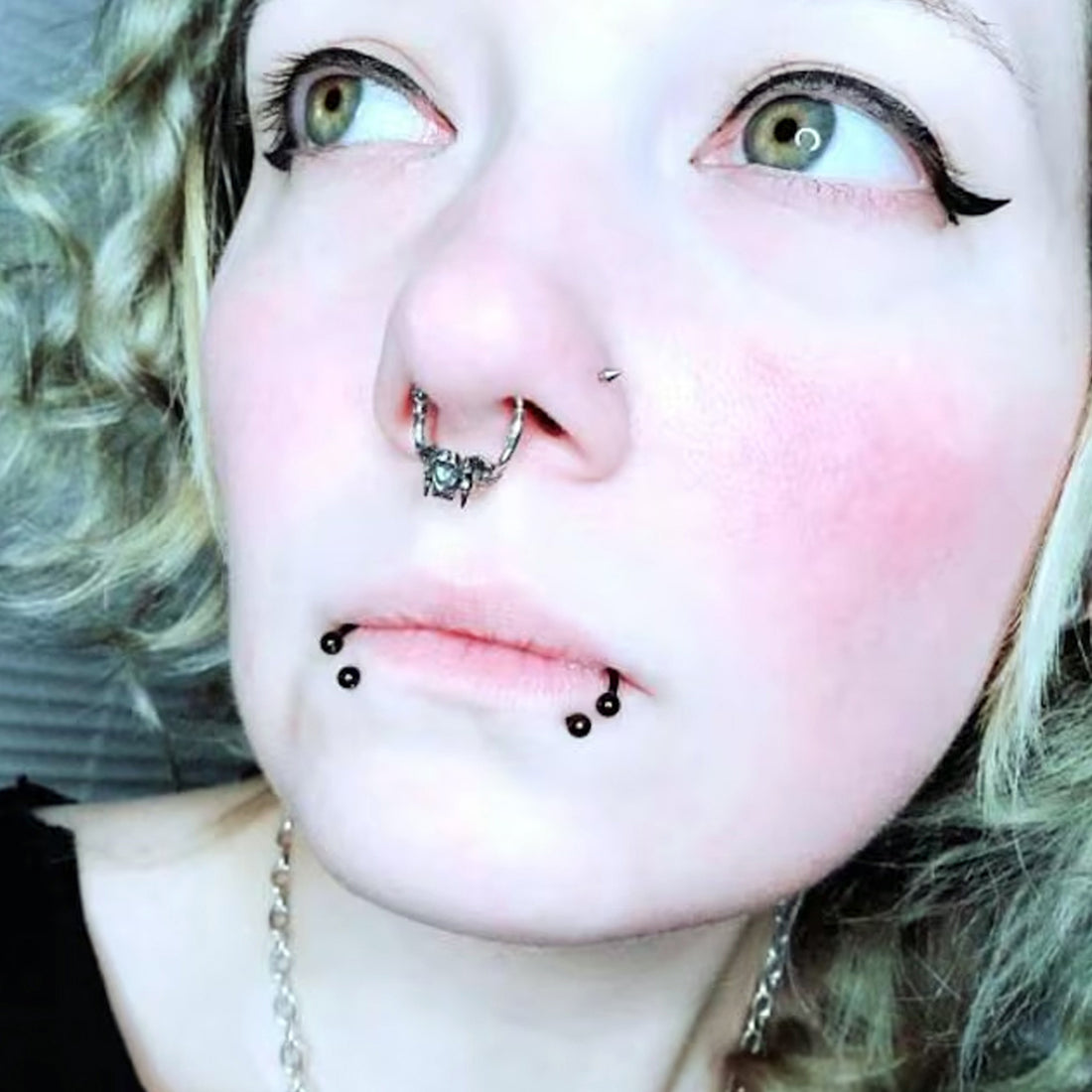 Sterling silver Gothic cat skull jaw septum clicker ring by RBZ Jewelry, worn by a female model with blonde hair, winged eyeliner, and multiple facial piercings to show real-world fit and style.