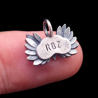 A detailed macro photograph of the rear view of the Sterling Silver Gothic Moon Owl pendant from RBZ Jewelry, held on a fingertip for scale. The image shows the stamped "RBZ" maker's mark on the central body plate, which is flanked by intricately textured and oxidized silver feathers, all against a solid black background.
