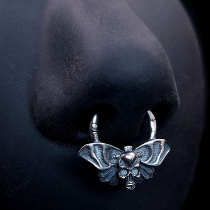 Sterling silver Gothic Death Moth septum clicker, by RBZ Jewelry,  worn on a black life-size silicone nose model, showcasing the symmetrical spread wings and skull motif in a realistic piercing placement.
