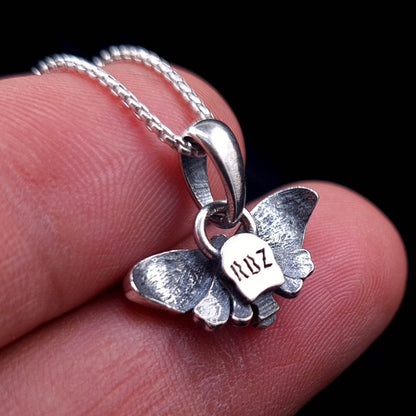 Back view of sterling silver Death Moth pendant held between fingers showing RBZ Jewelry logo engraving