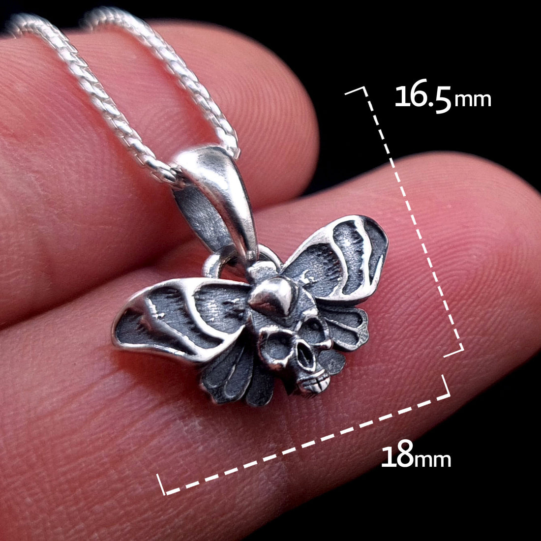 Sterling silver Death Moth pendant with skull detail, held for scale. White dotted lines indicate 18mm wing width and 16.5mm total height