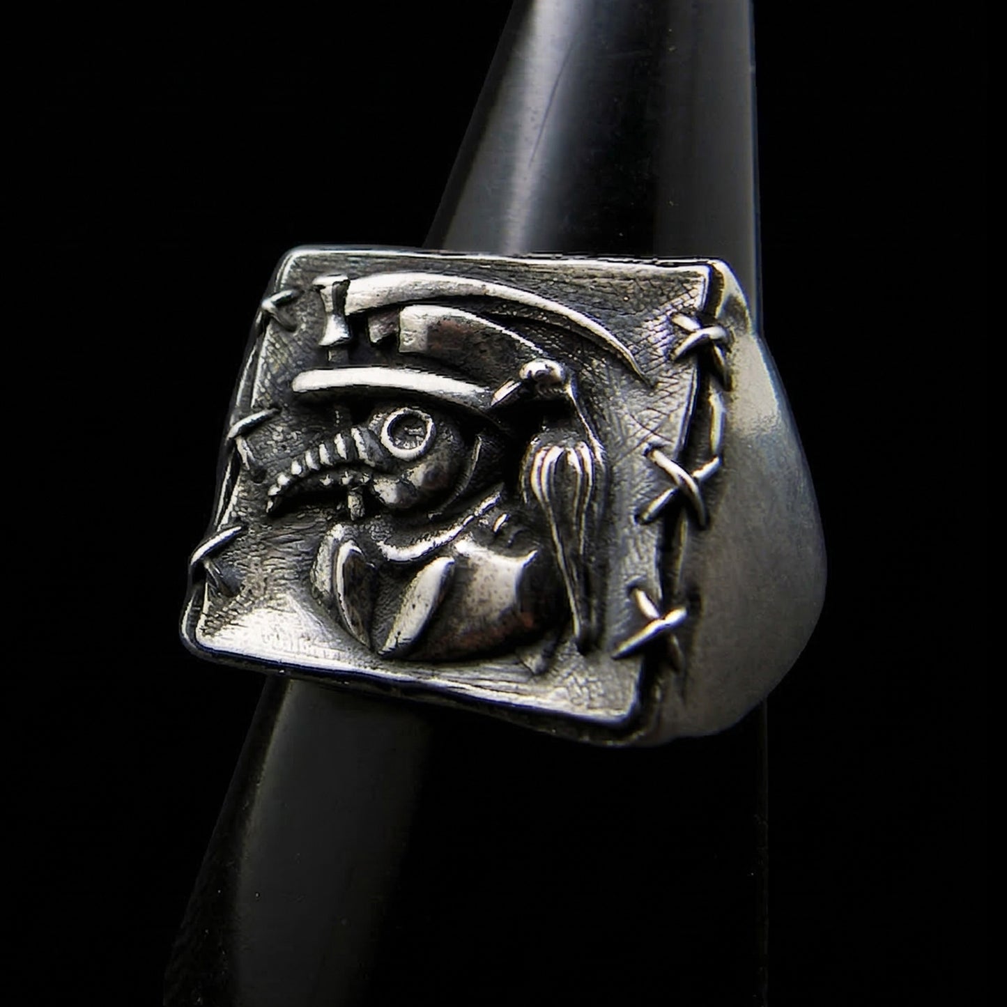 Sterling silver Plague Doctor signet ring by RBZ Jewelry featuring a high-relief sculpture of a beaked mask, raven, and sickle with hand-stitched border detailing.
