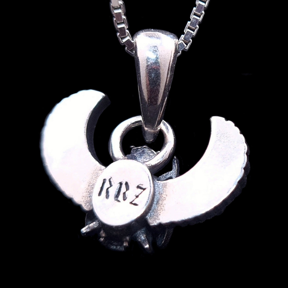 The reverse side of the sterling silver Gothic Egyptian Skull Scarab pendant by RBZ Jewelry, showcasing the back of the winged form on a solid black background. A central circular medallion features the distinct engraved brand logo 'RBZ' in a stylized font.