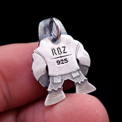 Back view of the handcrafted sterling silver Golem of Prague pendant by RBZ Jewelry, held on a finger for size reference. The oxidized silver surface features the engraved RBZ logo and 925 hallmark on the flat silhouette of the punk-rock guardian character.