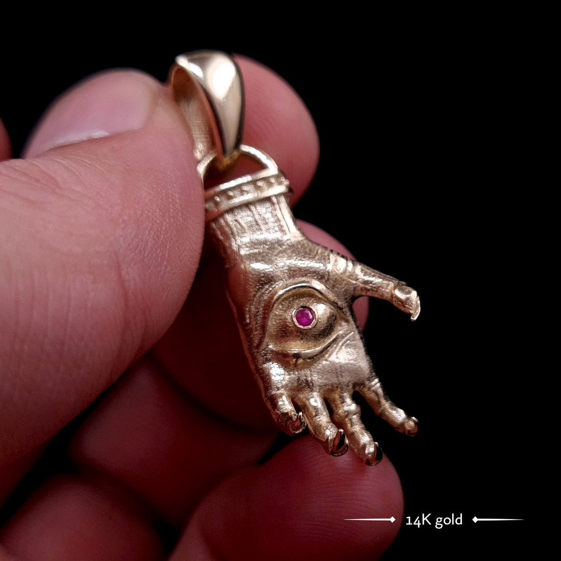 'The Nocturnal Hamsa' 14K Yellow Gold Pendant by RBZ Jewelry - Detailed Gothic clawed hand design featuring a central haunted eye set with a deep red faceted ruby gemstone. The sculpted gold has a textured finish with darkened recesses.