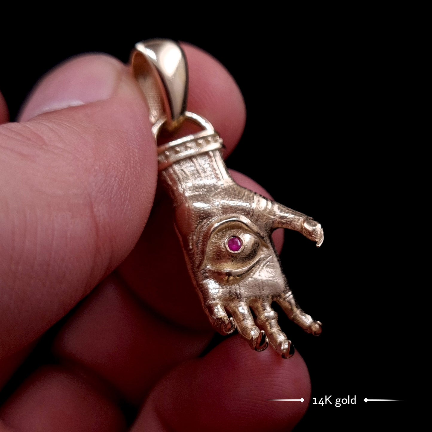 'The Nocturnal Hamsa' 14K Yellow Gold Pendant by RBZ Jewelry - Detailed Gothic clawed hand design featuring a central haunted eye set with a deep red faceted ruby gemstone. The sculpted gold has a textured finish with darkened recesses.