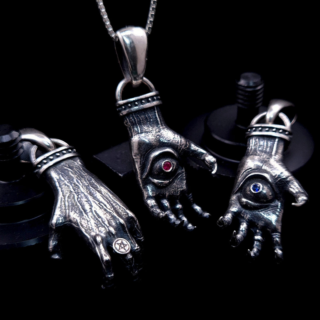 'The Nocturnal Hamsa' Sterling Silver Pendants Group Shot by RBZ Jewelry - Atmospheric display of three Gothic clawed hand designs featuring Ruby, Blue Sapphire, and a reversible back view with an intricate Pentagram ring.