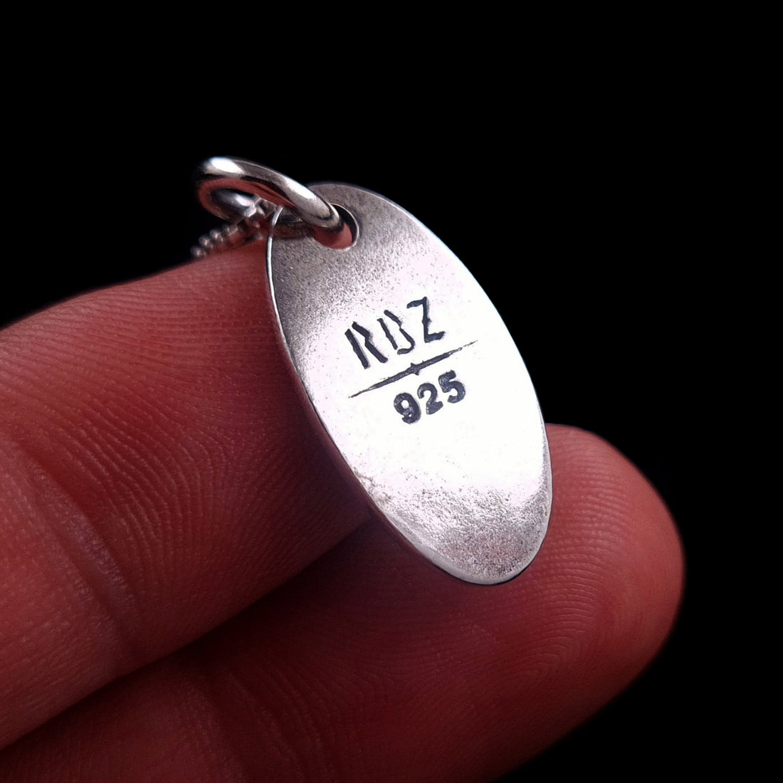 A hand holding the reverse side of the solid 925 sterling silver Hecate medallion to show scale and proportions, featuring the deep-engraved RBZ logo and hallmark on a weathered silver surface