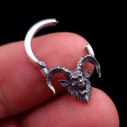 Sterling silver Horned Demon septum clicker ring by RBZ Jewelry held between fingers in the open position, showing the hinge mechanism and detailed gothic demon design against a black background.