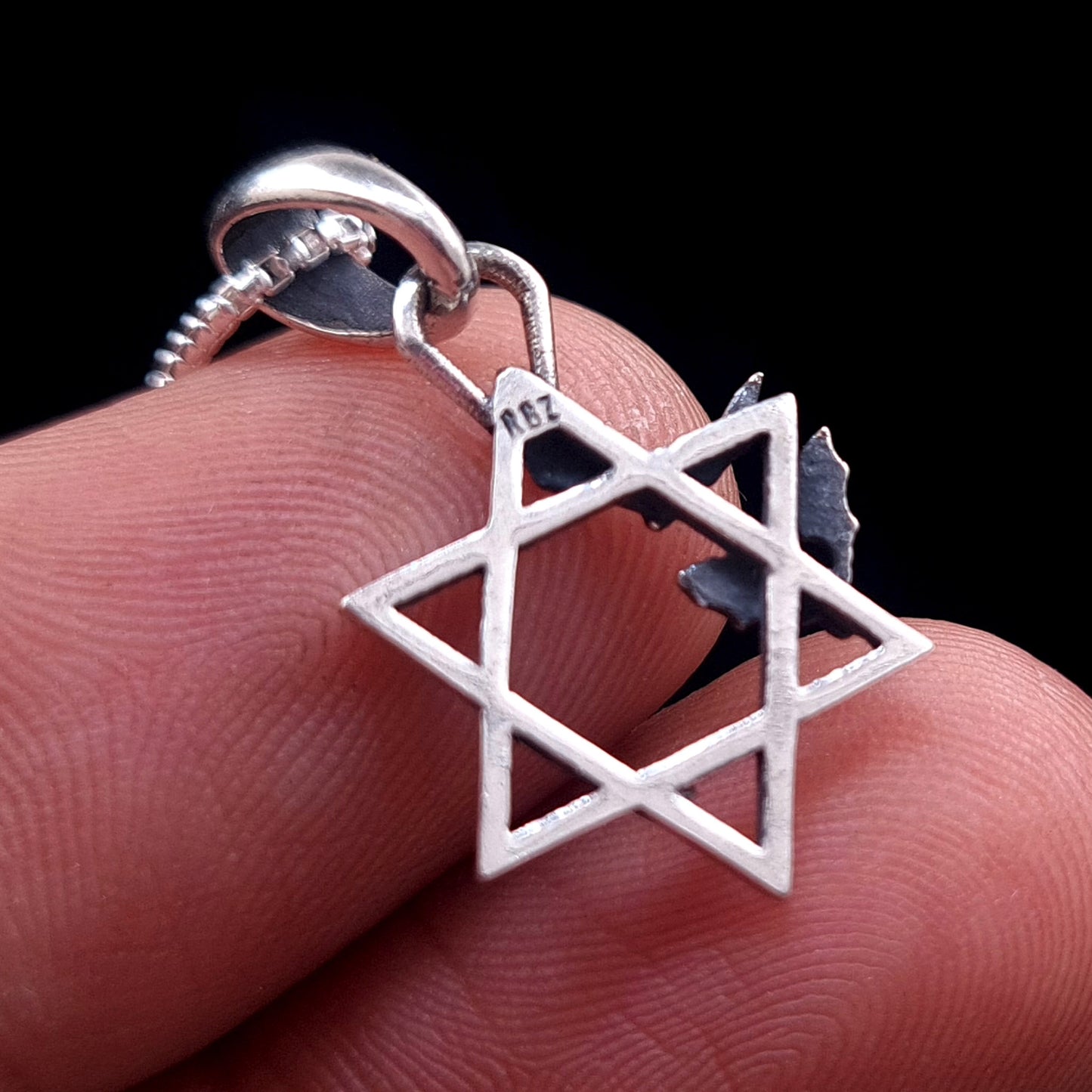 Back view of the sterling silver Bats Star of David pendant held between fingers for scale, showing the RBZ designer hallmark on the top point of the Magen David, by RBZ Jewelry.