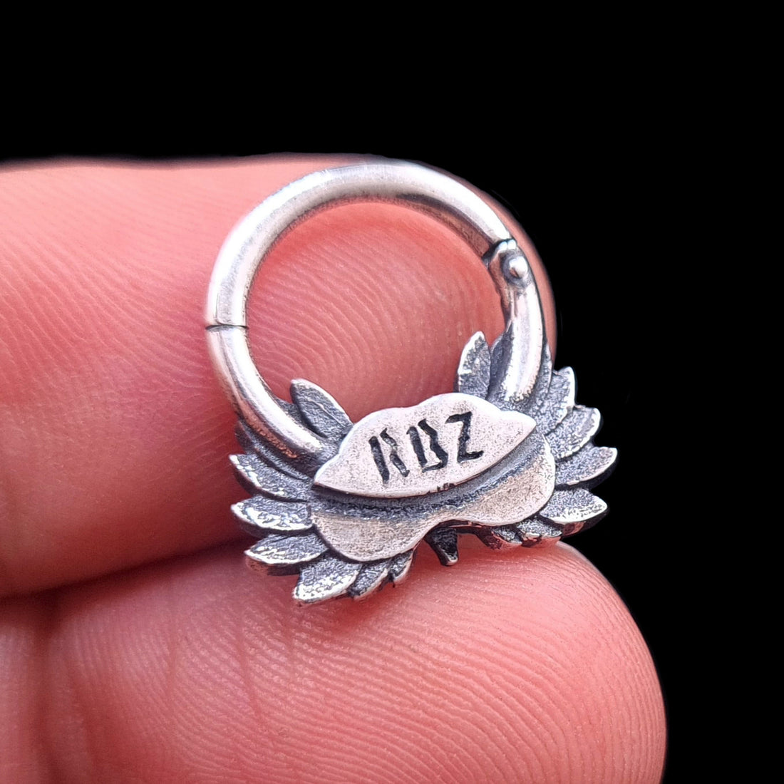 Handheld back view of the Sterling silver Moon Owl septum ring by RBZ Jewelry, highlighting the RBZ brand engraving on the reverse side of the owl design. The oxidized gothic septum clicker is held between fingers against a black background.