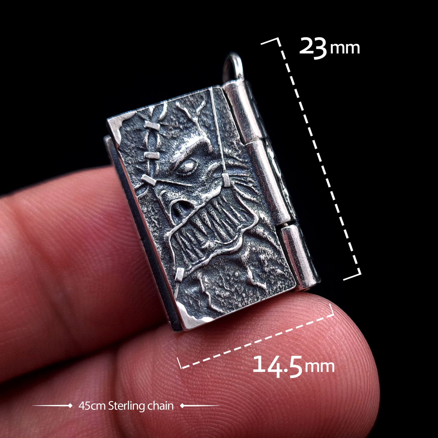 A detailed front view of the sterling silver Necronomicon book locket held between two fingers, featuring white text overlays indicating its dimensions: 23mm in height and 14.5mm in width. The bottom of the image notes a 45cm Sterling chain. The oxidized silver cover shows a visceral skeletal face with stitched skin textures, highlighting the compact scale and gothic horror craftsmanship of the RBZ Jewelry pendant against a black background.