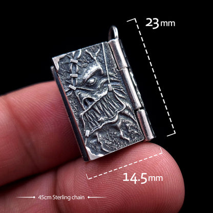 A detailed front view of the sterling silver Necronomicon book locket held between two fingers, featuring white text overlays indicating its dimensions: 23mm in height and 14.5mm in width. The bottom of the image notes a 45cm Sterling chain. The oxidized silver cover shows a visceral skeletal face with stitched skin textures, highlighting the compact scale and gothic horror craftsmanship of the RBZ Jewelry pendant against a black background.