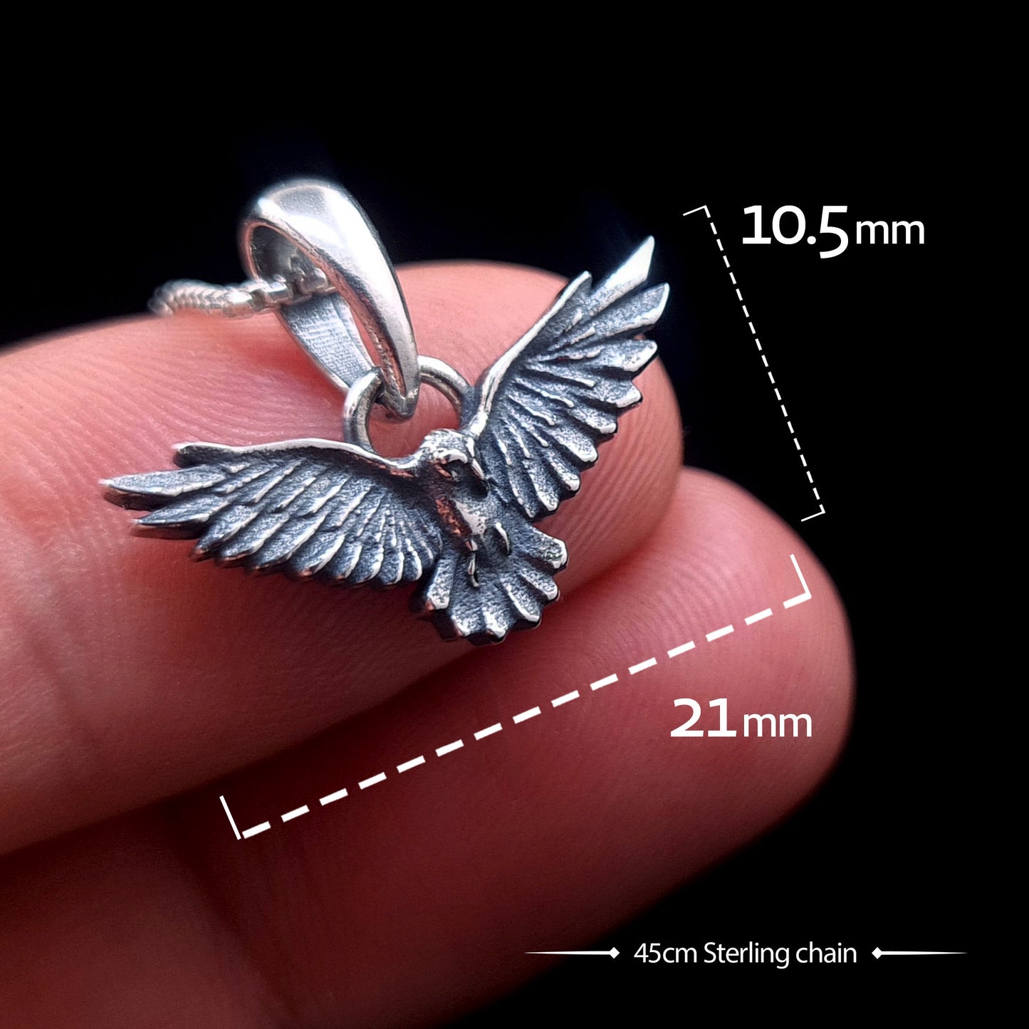 Sterling silver flying raven pendant held on fingers for scale demonstration, showing dimensions of 21mm width and 10.5mm height with a 45cm sterling chain, Gothic crow necklace by RBZ Jewelry.