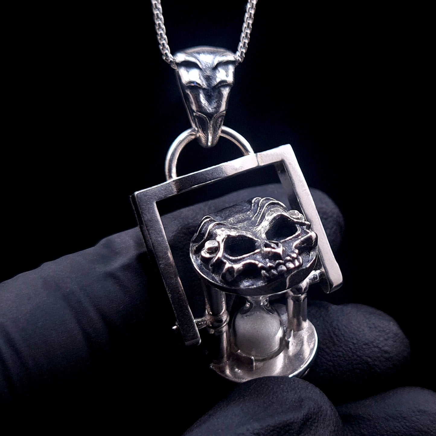 A proportional view of the Rotating Skull Hourglass Pendant held in hand to show size. Handcrafted in Solid 925 Sterling Silver with a kinetic biomechanical skull cap and functional sand timer by RBZ Jewelry.