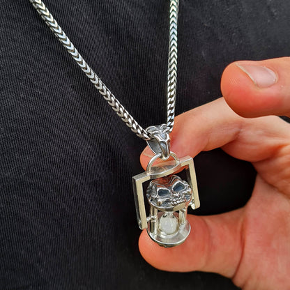 Close-up of a male model holding the kinetic Rotating Skull Hourglass Pendant between two fingers to demonstrate its physical proportions. Handcrafted in solid 925 sterling silver with biomechanical detailing by RBZ Jewelry.