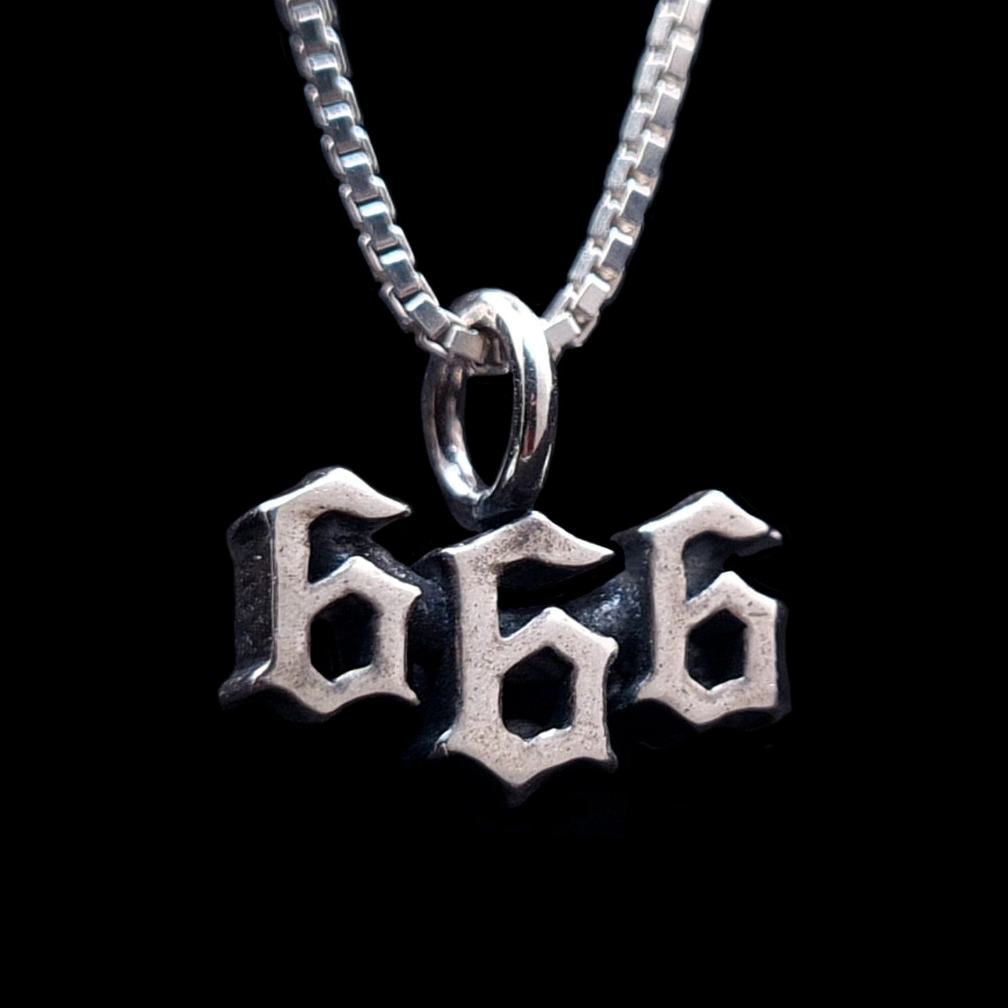 Front-right view of the Sterling silver 666 pendant by RBZ Jewelry, featuring a sharp Gothic font and an oxidized finish, hanging from a silver box chain against a black background.