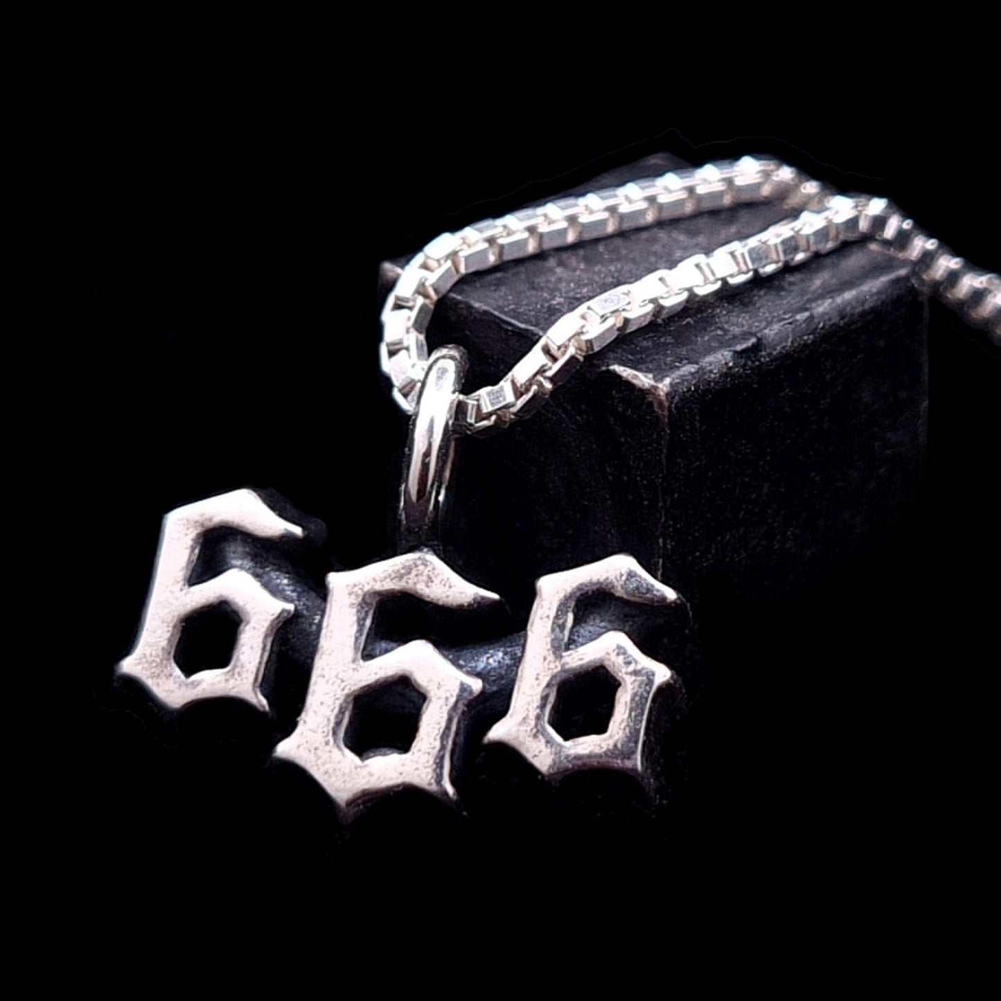 Dainty Sterling silver Satanic 666 pendant with a Gothic font and oxidized finish by RBZ Jewelry, displayed on a silver box chain against a dark background.