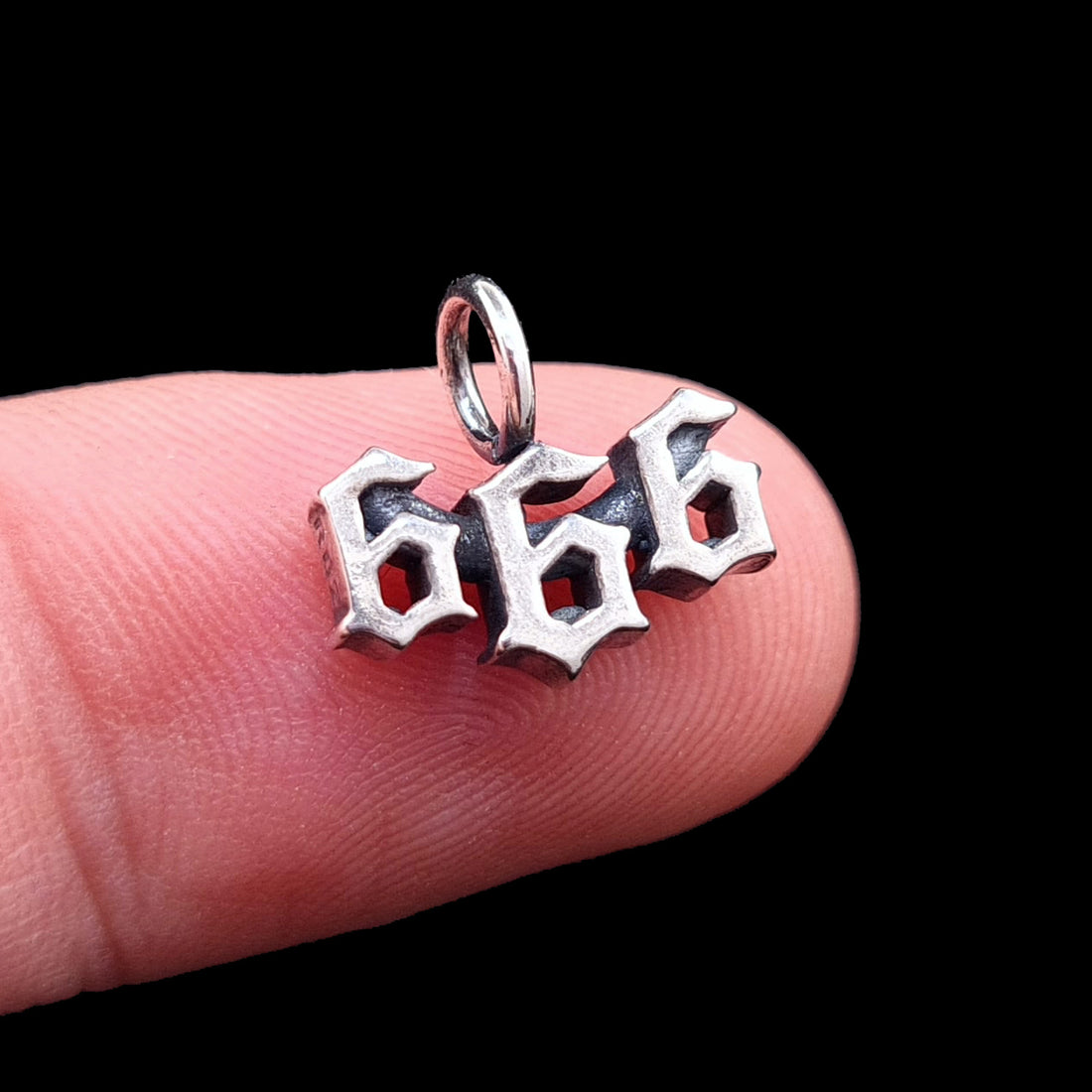 Sterling silver 666 Number of the Beast pendant by RBZ Jewelry held on a finger for scale, featuring a dainty Gothic font and dark oxidized finish.